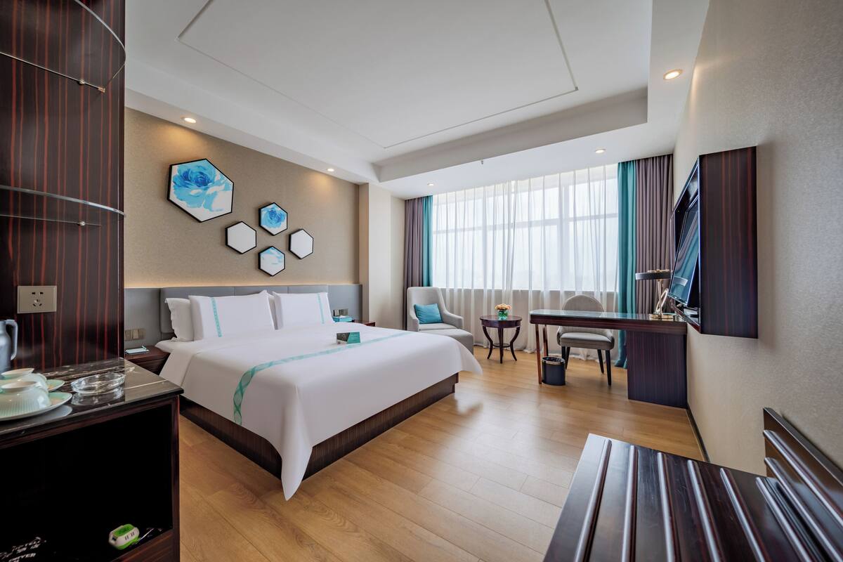 Ein Hotelzimmer mit einem großen Bett, einem Schreibtisch, einem Stuhl, einem Fernseher und einem Fenster mit Vorhängen.