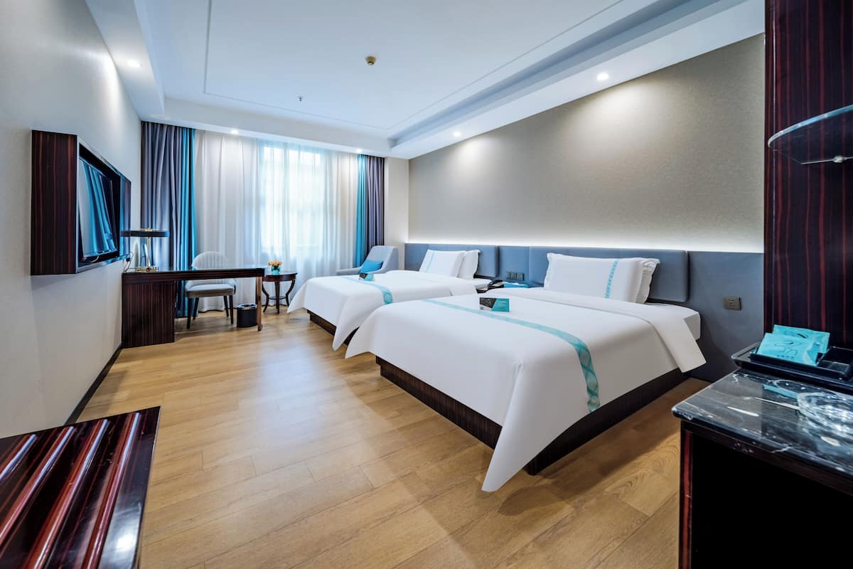 Ein Hotelzimmer mit zwei Betten, einem Schreibtisch, einem Sessel, einem Fernseher und einer Minibar.