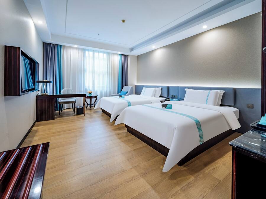 A hotel room with two beds, a desk, a chair, a TV, and a minibar.