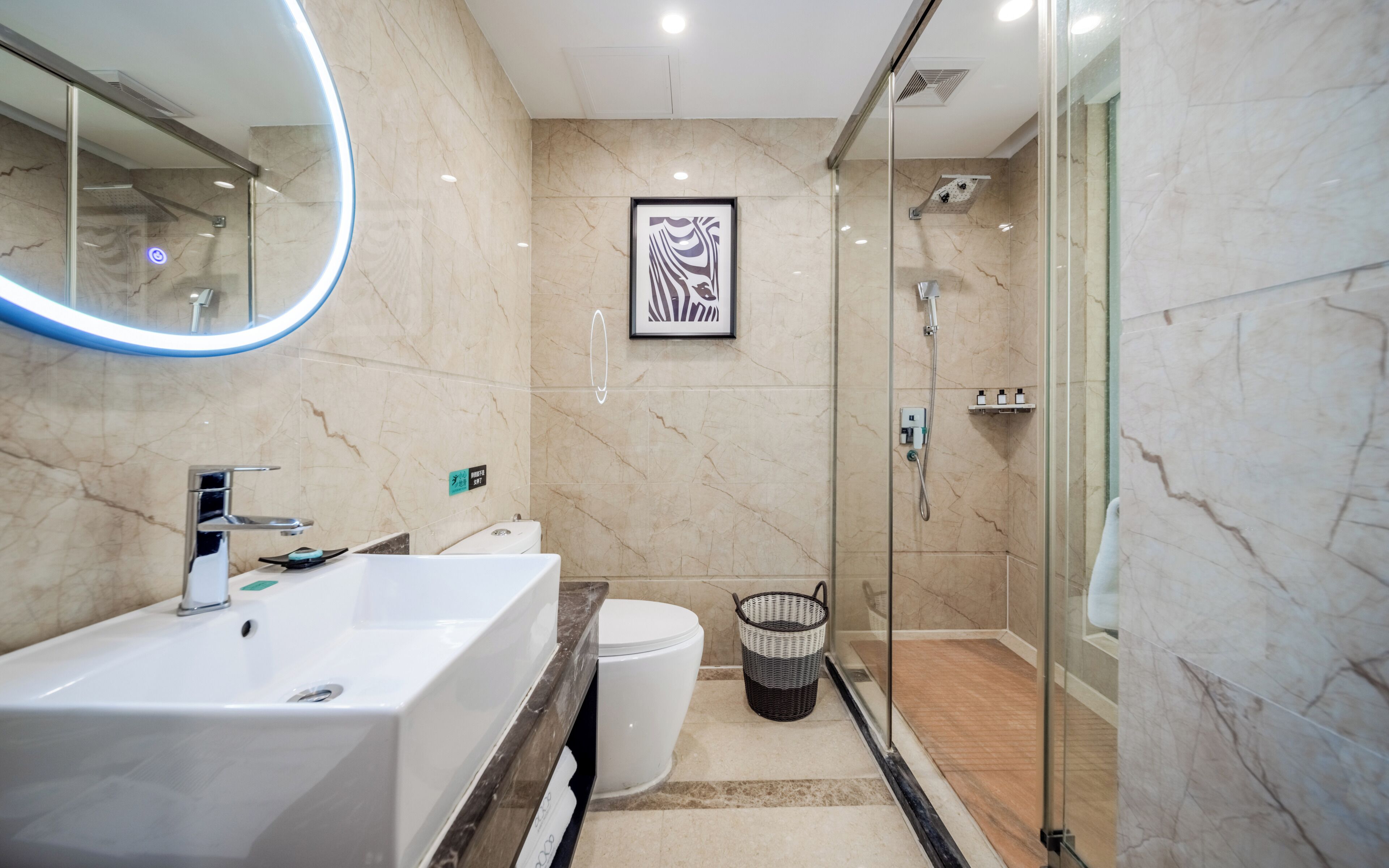 Un baño moderno con un lavamanos grande de color blanco, una cabina de ducha de vidrio y una obra de arte enmarcada en la pared.