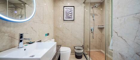 Un baño moderno con un lavamanos grande de color blanco, una cabina de ducha de vidrio y una obra de arte enmarcada en la pared.