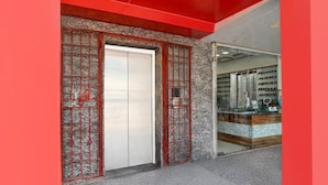 A modern building entrance with a red facade, a glass door, and a visible interior with shelves and items. - Hotel O Deendayal Crossway Ranchi (Ranchi)