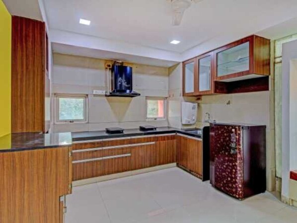 A compact kitchen with wooden cabinets, a built-in microwave, and a refrigerator. - Super Collection O Vardhan House (Pune)