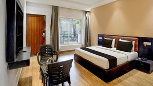 Ein Hotelzimmer mit Bett, Schreibtisch, zwei Stühlen, Fernseher und einem Vorhangfenster.