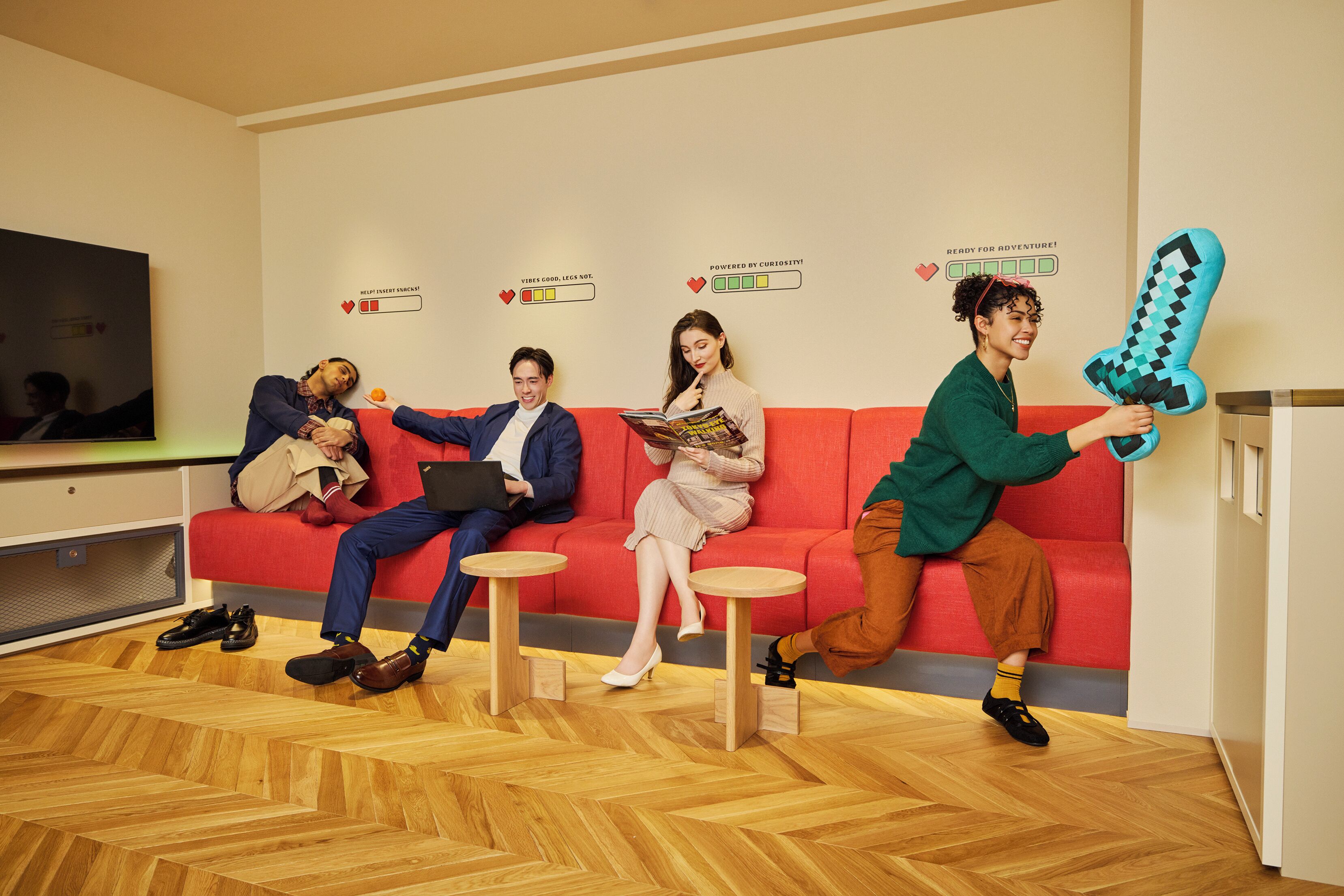 A modern waiting area with a red couch, wooden floor, and a person holding a large cushion.