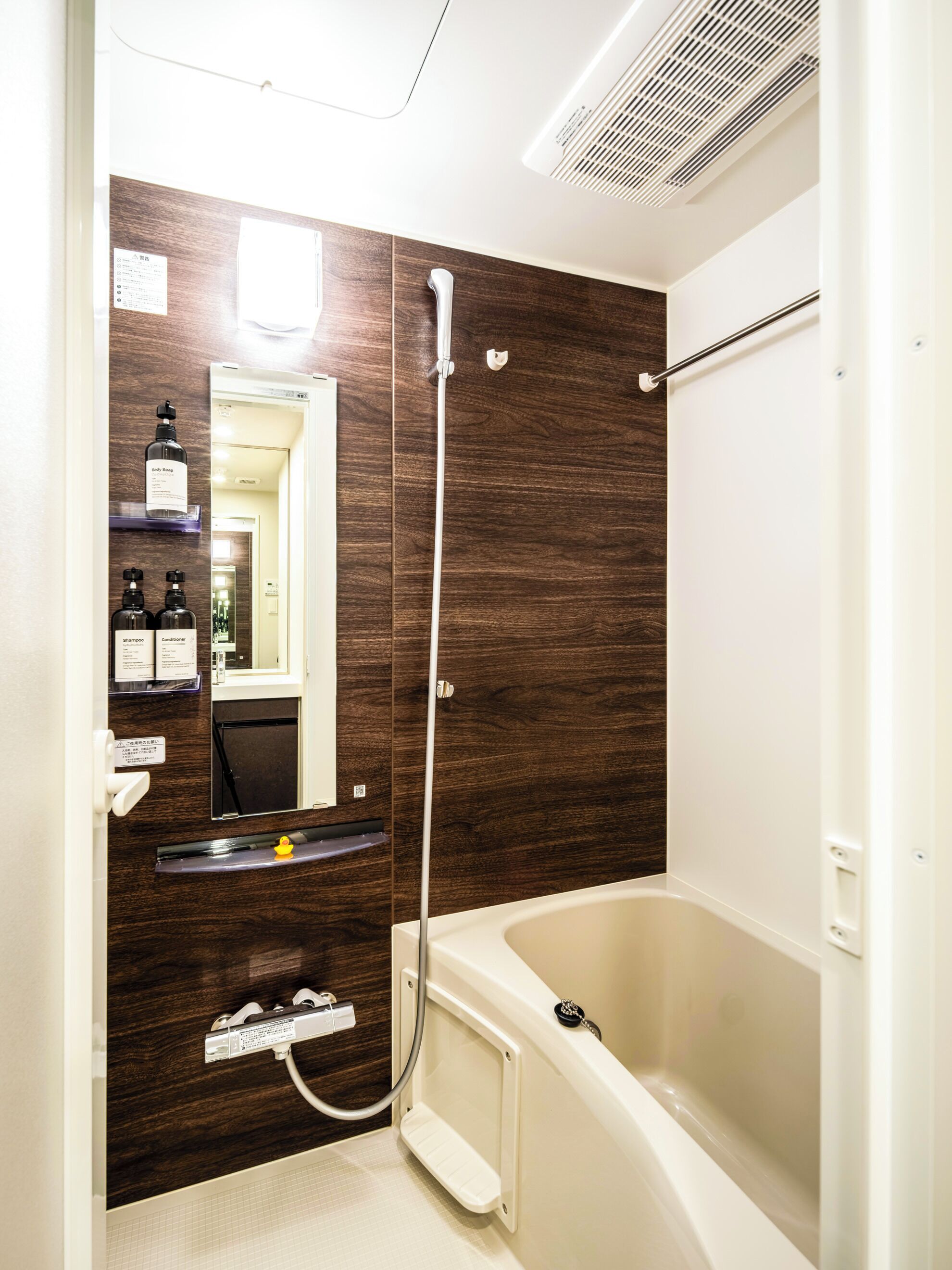 A modern bathroom with a bathtub, a shower, and a vanity with a mirror. There are toiletries on the shelf.