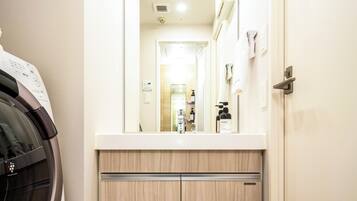 A compact laundry area with a washing machine, a countertop, and a mirror reflecting a bathroom with a sink and towel rack.