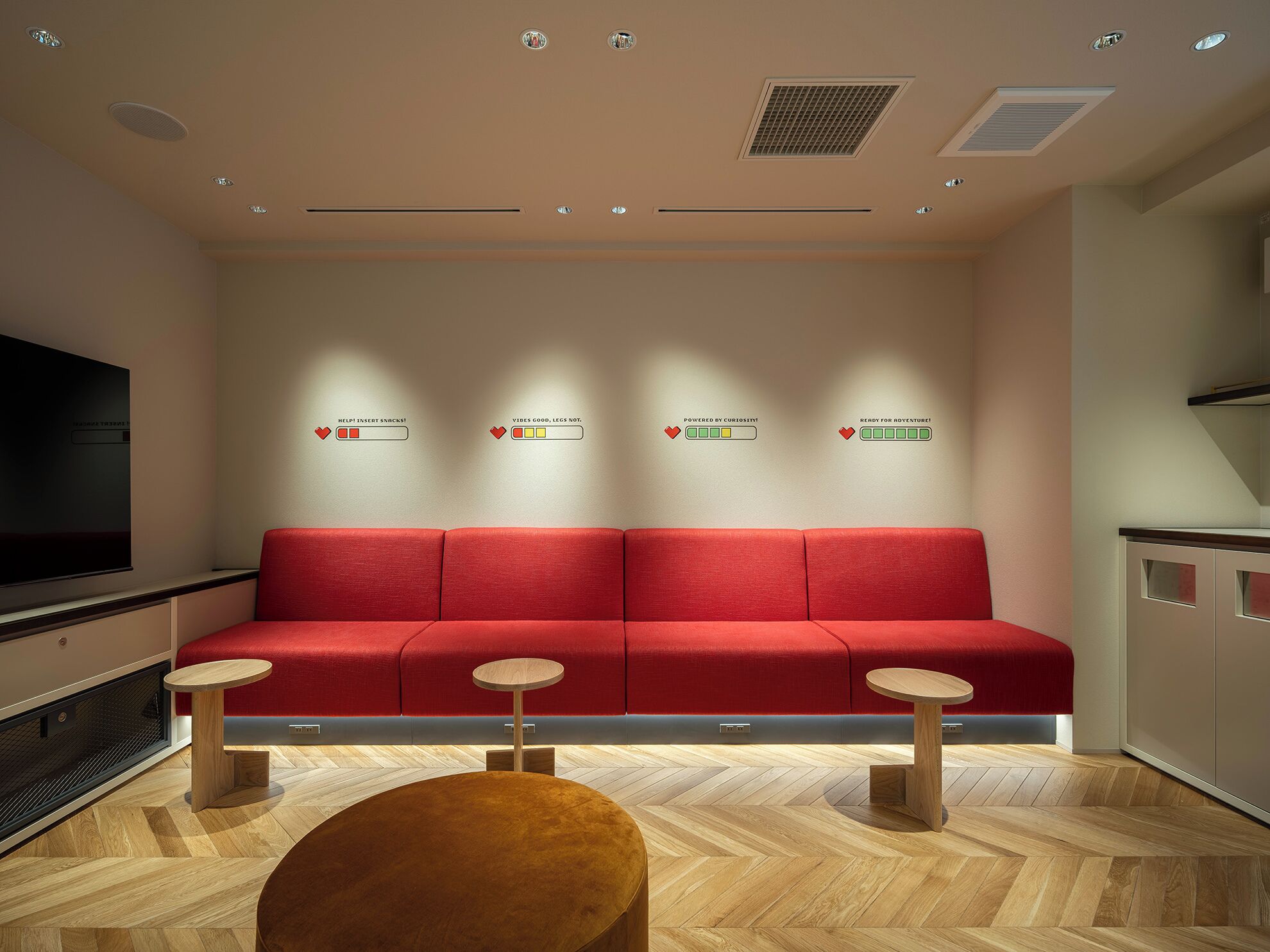 A modern waiting area with a red sofa, two small tables, and a large TV screen.