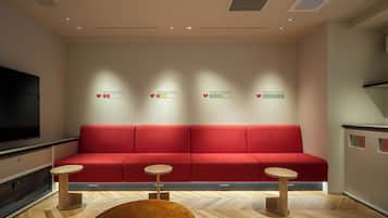 A modern waiting area with a red sofa, two small tables, and a large TV screen.