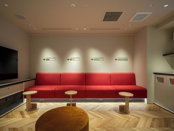 Un espace d’attente moderne avec un canapé rouge, deux petites tables et un grand écran de télévision.