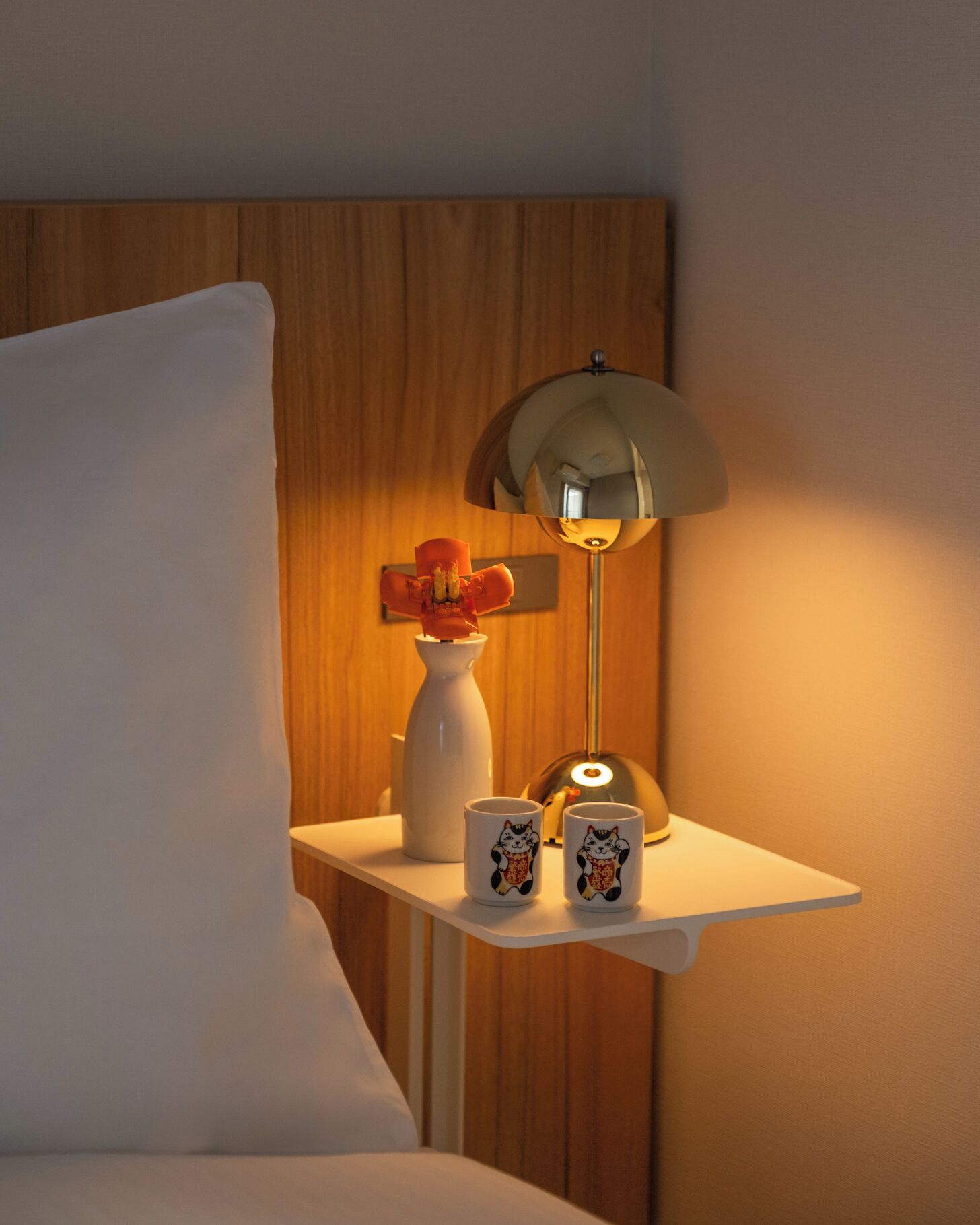 A bedside table with a lamp, a vase with flowers, and two mugs with cat designs.