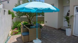 En patio med blå parasol, fletmøbler og krukker med planter.