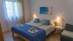 Un letto matrimoniale con copriletto blu, due comodini con lampade, un divano grigio e un quadro appeso al muro.