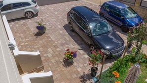 Un'area di parcheggio con due auto, una berlina bianca e un furgone blu, e diverse piante in vaso fiorite.