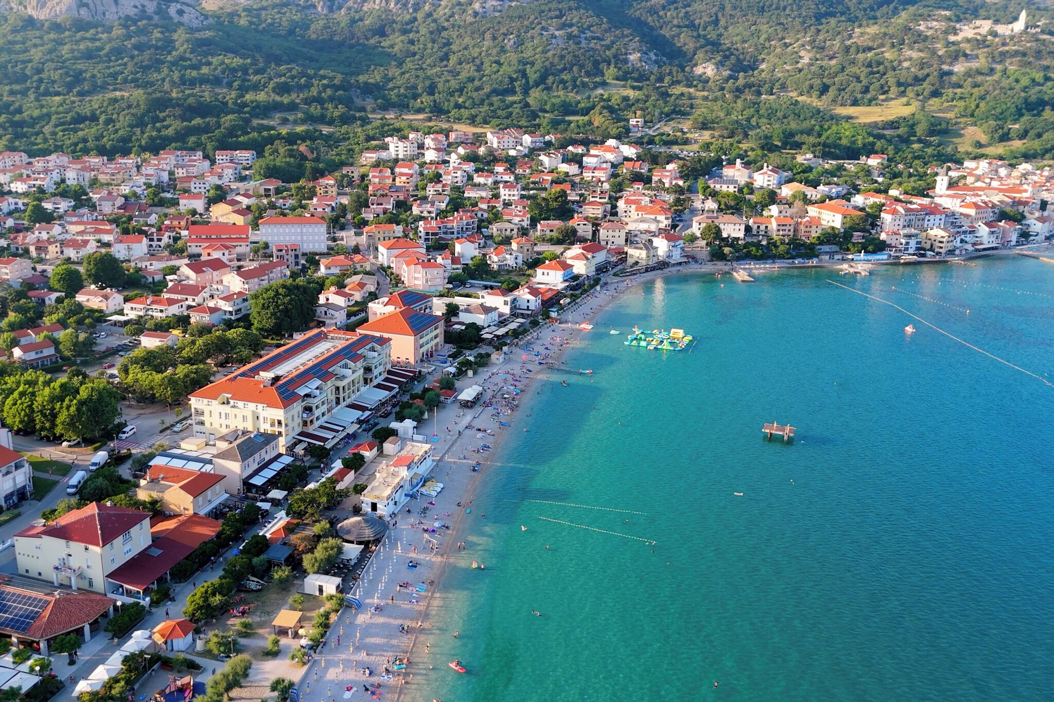 Vista aèria d'una població costanera amb platja, edificis i mar blau clar.