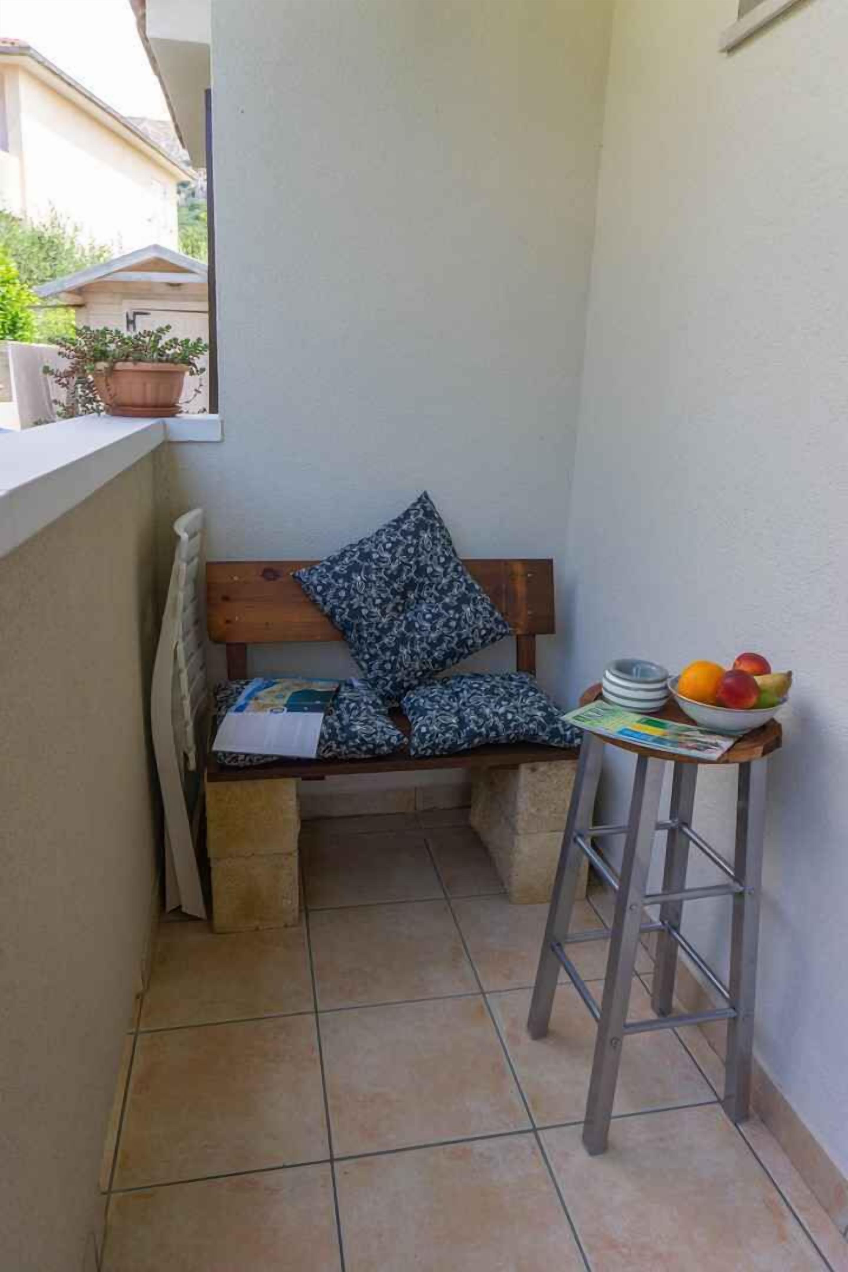 Un petit balcon avec un banc en bois, une plante en pot, un panier de fruits et un journal.