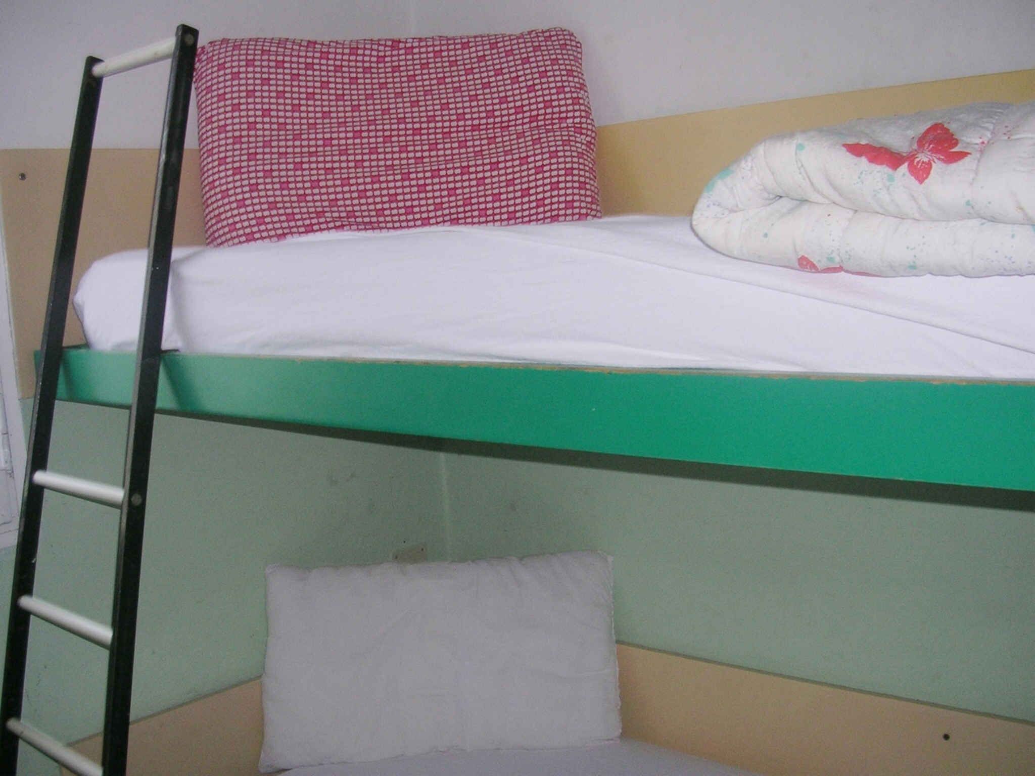 Un letto a castello con una scala, un cuscino rosso e bianco a quadri e una coperta bianca con un motivo floreale rosso.