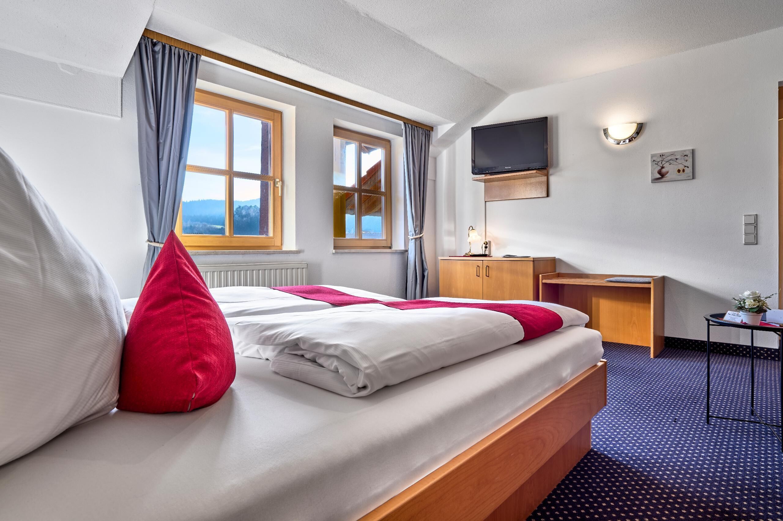 A hotel room with a bed, a desk, a TV, and a window with curtains.