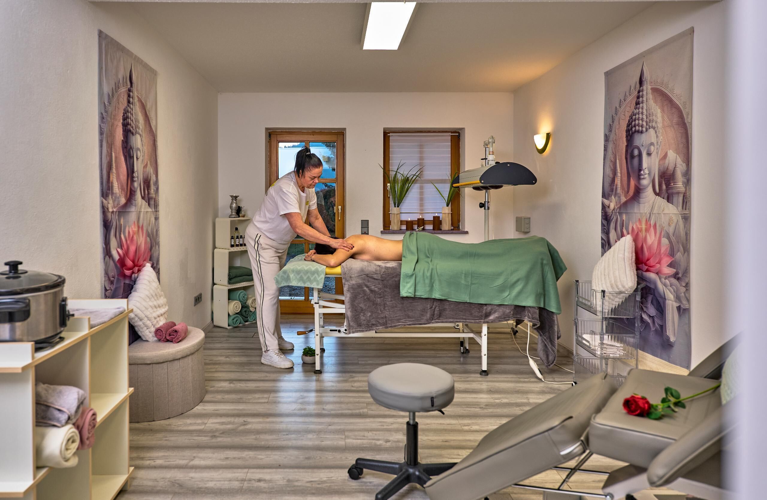 Un cuarto de terapia de masajes con una camilla, un terapeuta y un cliente recibiendo un masaje en la espalda.