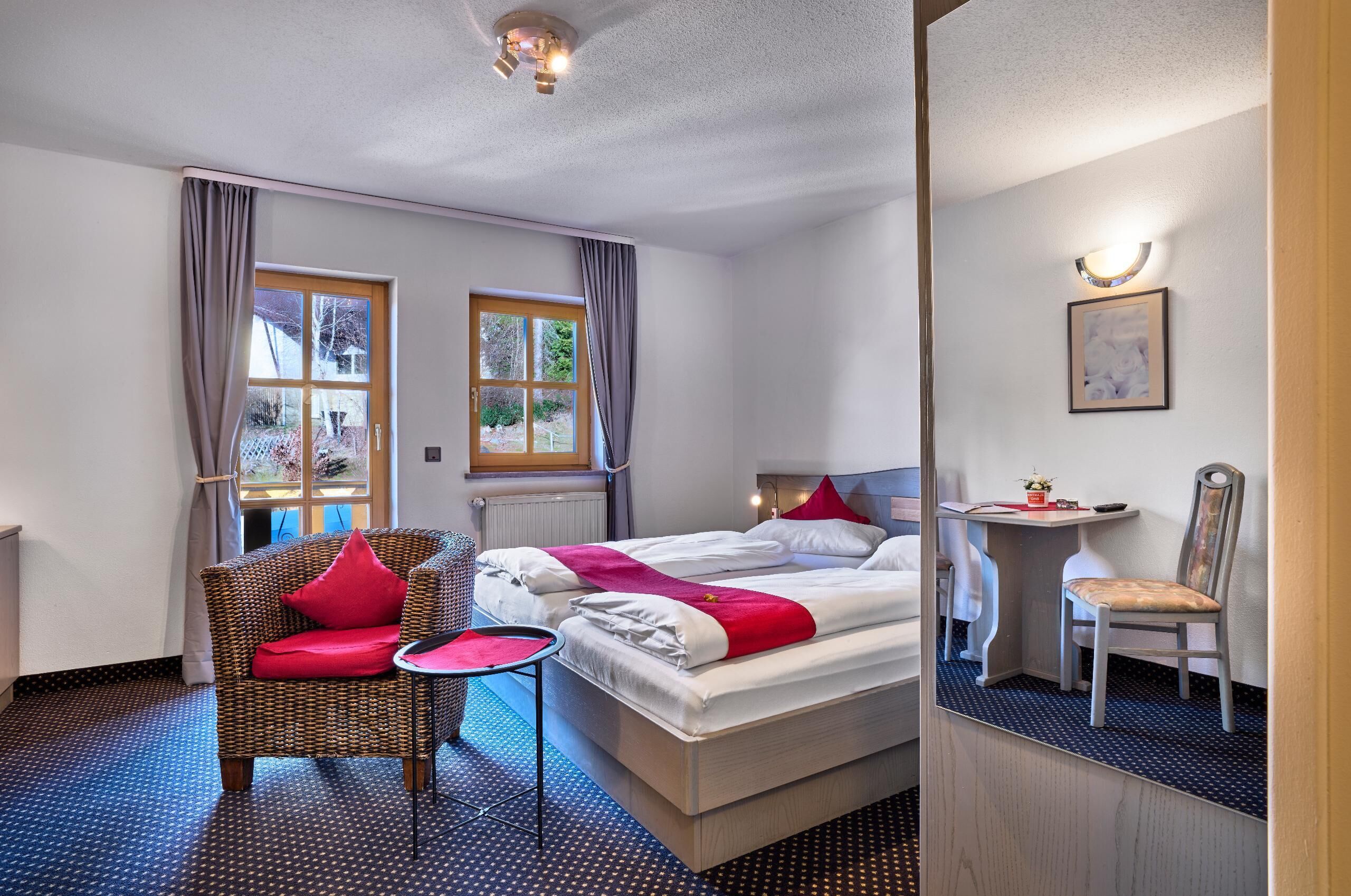 Ein Hotelzimmer mit zwei Betten, einem Sessel, einem kleinen Tisch und einem Spiegel.