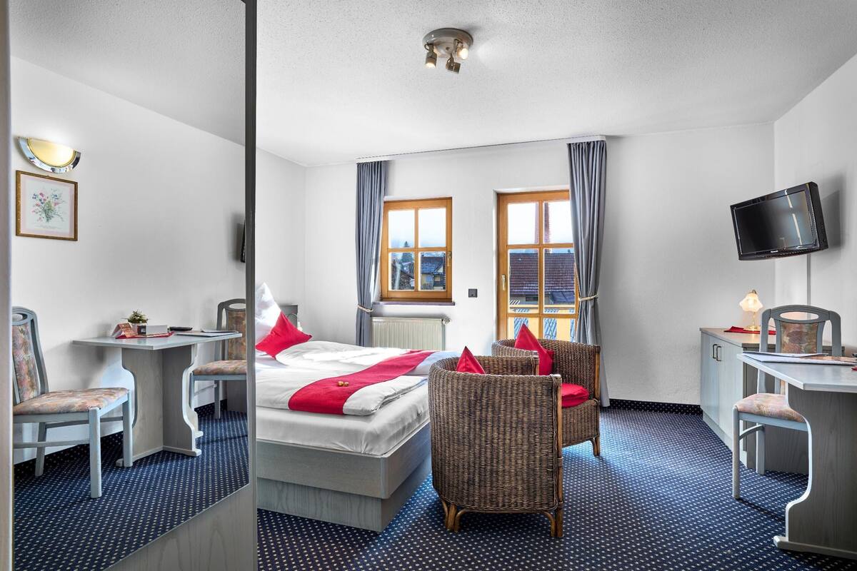 A hotel room with a bed, two chairs, a desk, a television, and a window with curtains.