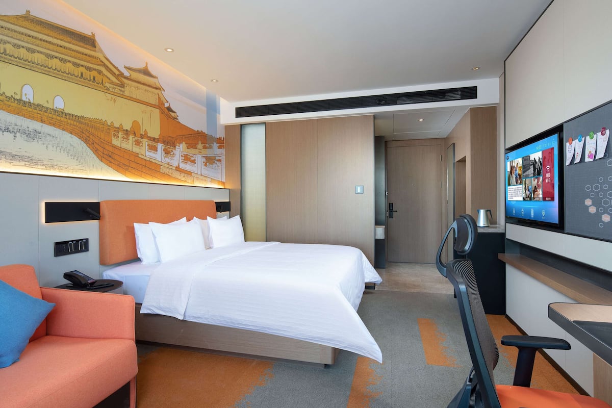 Una camera d'albergo con un letto, una scrivania, una sedia, una TV e un affresco sulla parete.