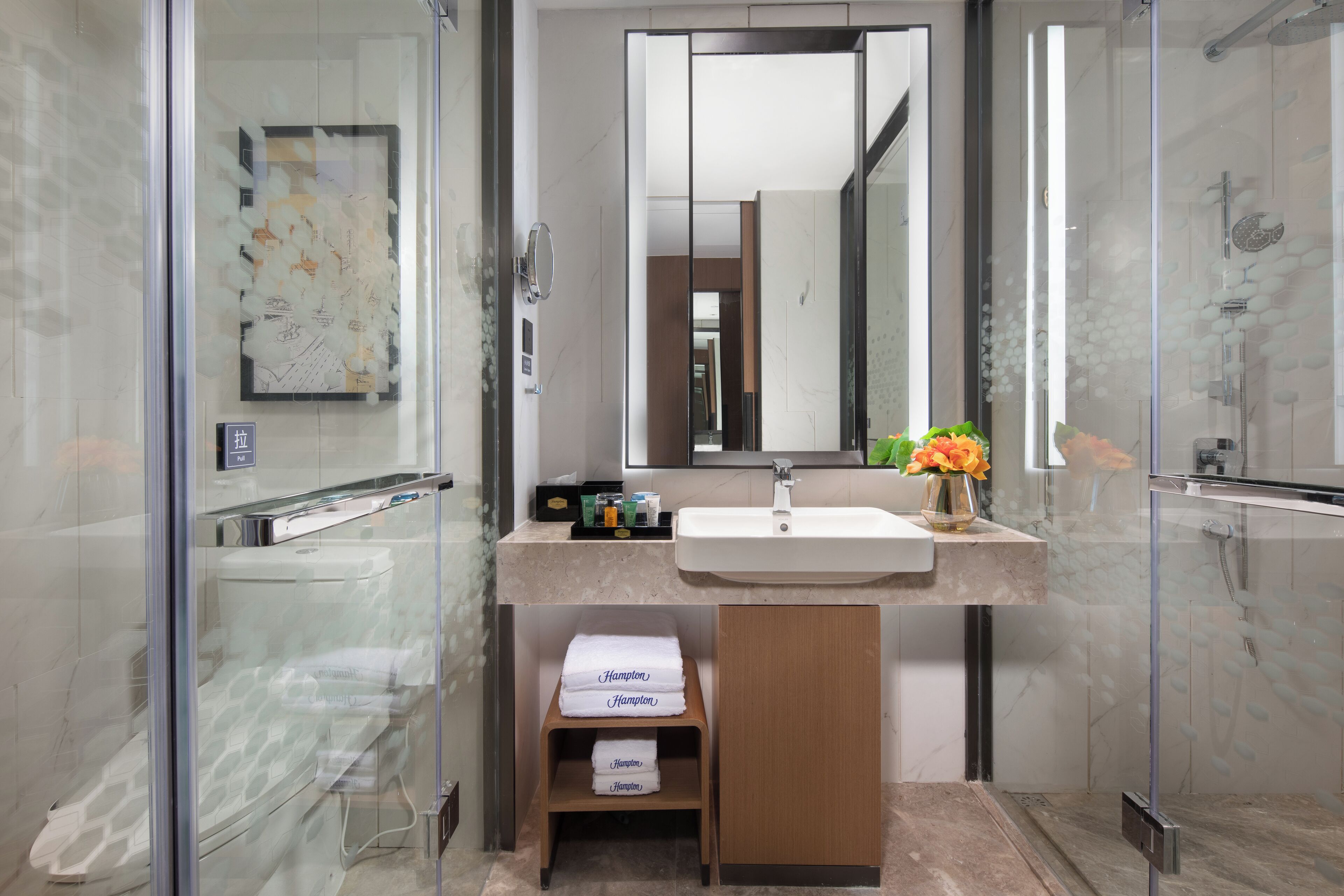 A modern bathroom with a glass shower enclosure, a large mirror, and a vanity with a sink and towel storage.