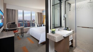 A hotel room with a bed, a desk, a large window with a city view, a bathroom with a mirror, sink, and shower. - Hampton by Hilton Beijing Wuzi Xueyuan Road (Tongzhou)