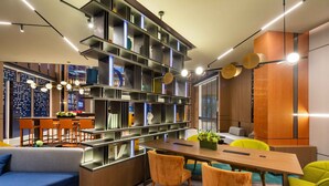 A modern interior with a wooden dining table, orange chairs, a blue sofa, and a large bookshelf. - Hampton by Hilton Beijing Wuzi Xueyuan Road (Tongzhou)