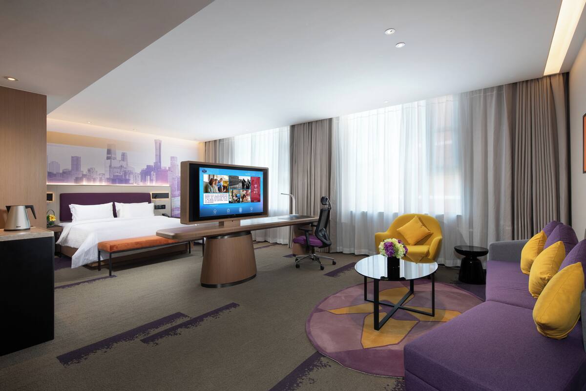 Una moderna camera d'hotel con un letto, una scrivania con un computer, una televisione, un divano e vista sulla città.