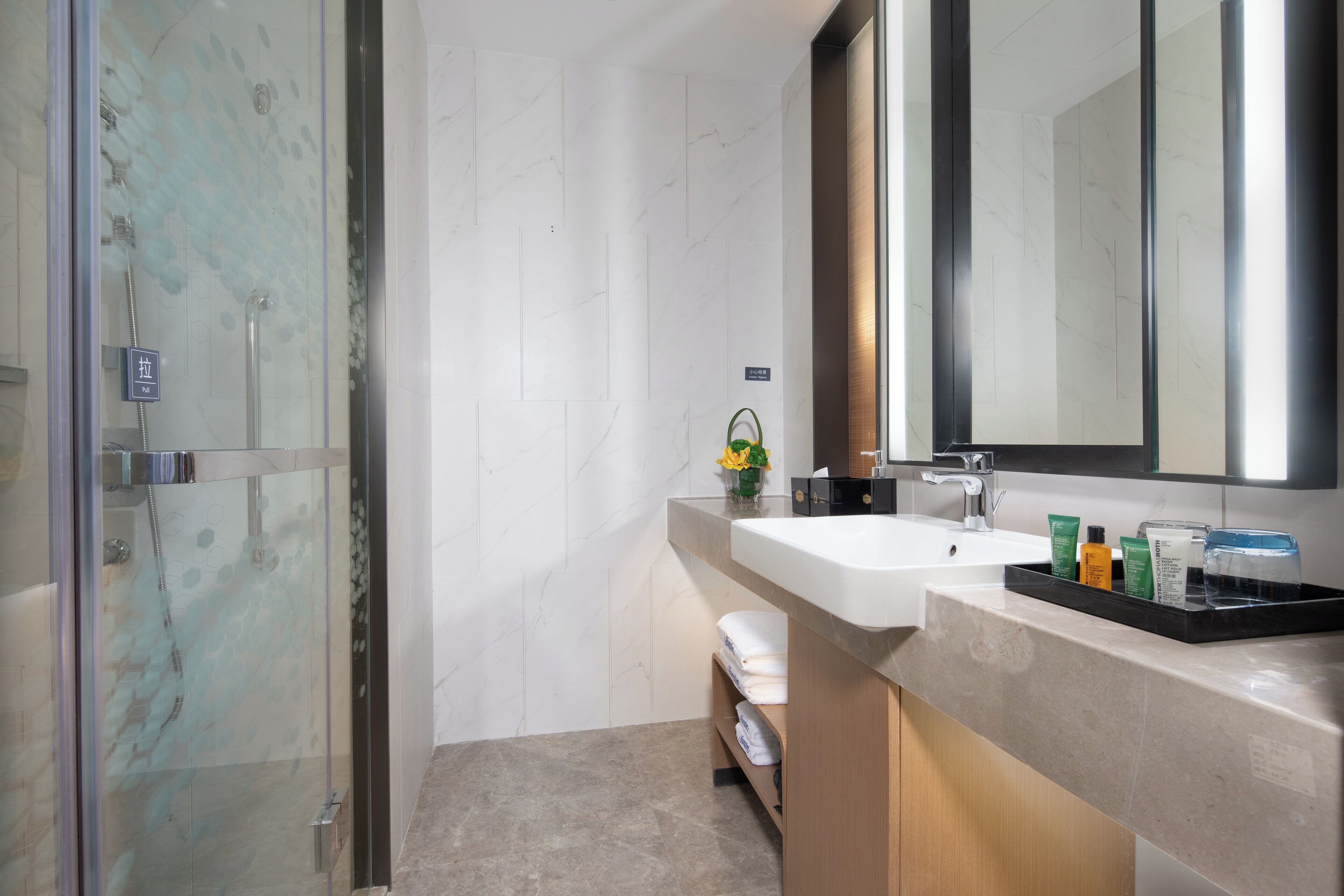 A modern bathroom with a glass shower enclosure, a sink with toiletries, and a mirror above the sink.
