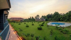 A hotel with a swimming pool, well-manicured lawn, and a view of the surrounding greenery. - Corbett Virasat by Vatsam Resorts (Kaladhungi)
