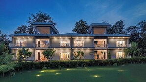 A two-story house with multiple balconies, large windows, and a well-lit exterior at dusk. - Corbett Virasat by Vatsam Resorts (Kaladhungi)