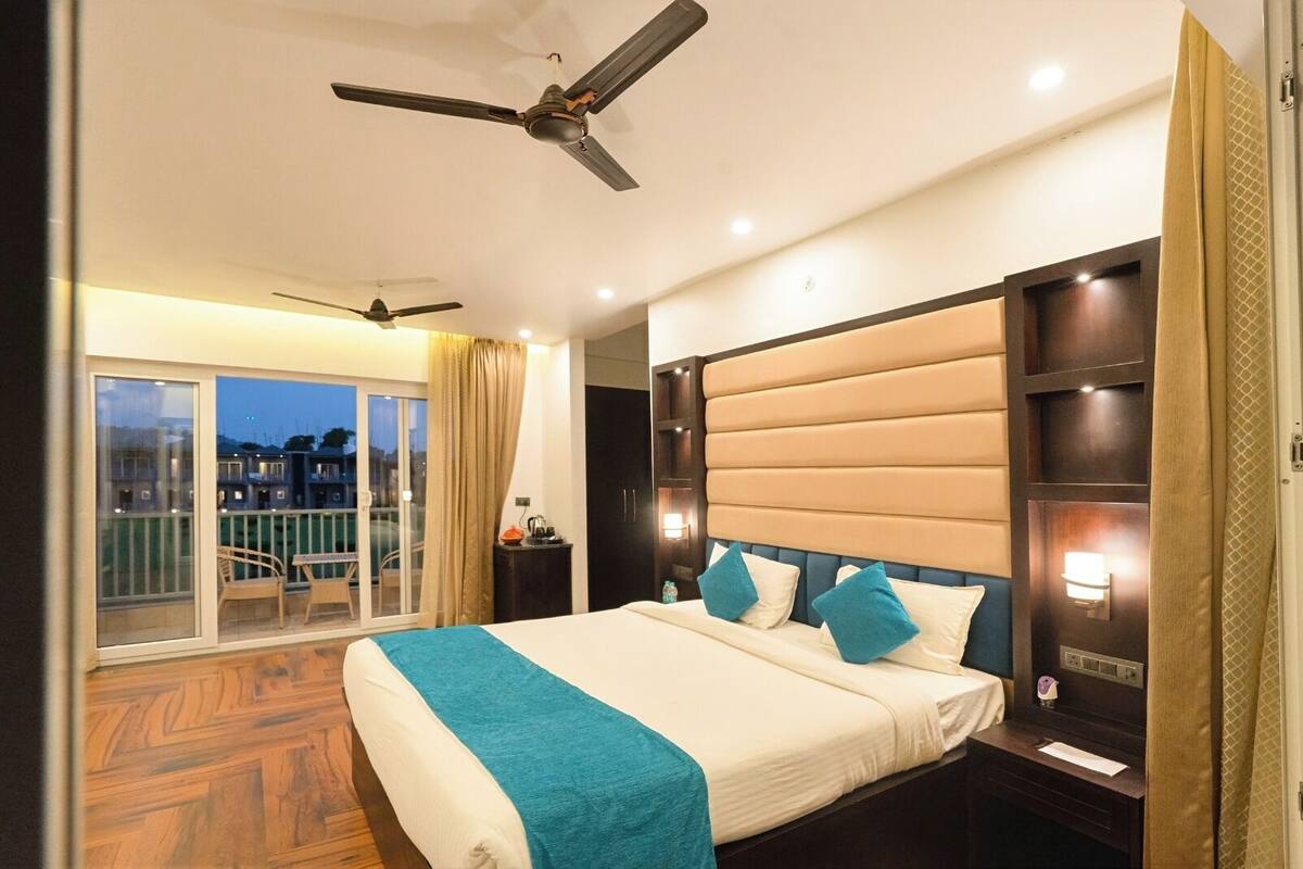 Une chambre d’hôtel avec un grand lit, un ventilateur de plafond, une table de chevet et une vue sur la ville depuis les portes du balcon.