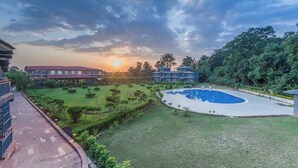 A resort with a swimming pool, well-maintained lawns, and buildings with balconies. - Corbett Virasat by Vatsam Resorts (Kaladhungi)