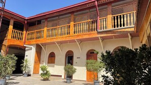 Un edificio tradicional con un patio central, con balcones de madera y barandillas de celosía, arcos y macetas con plantas.