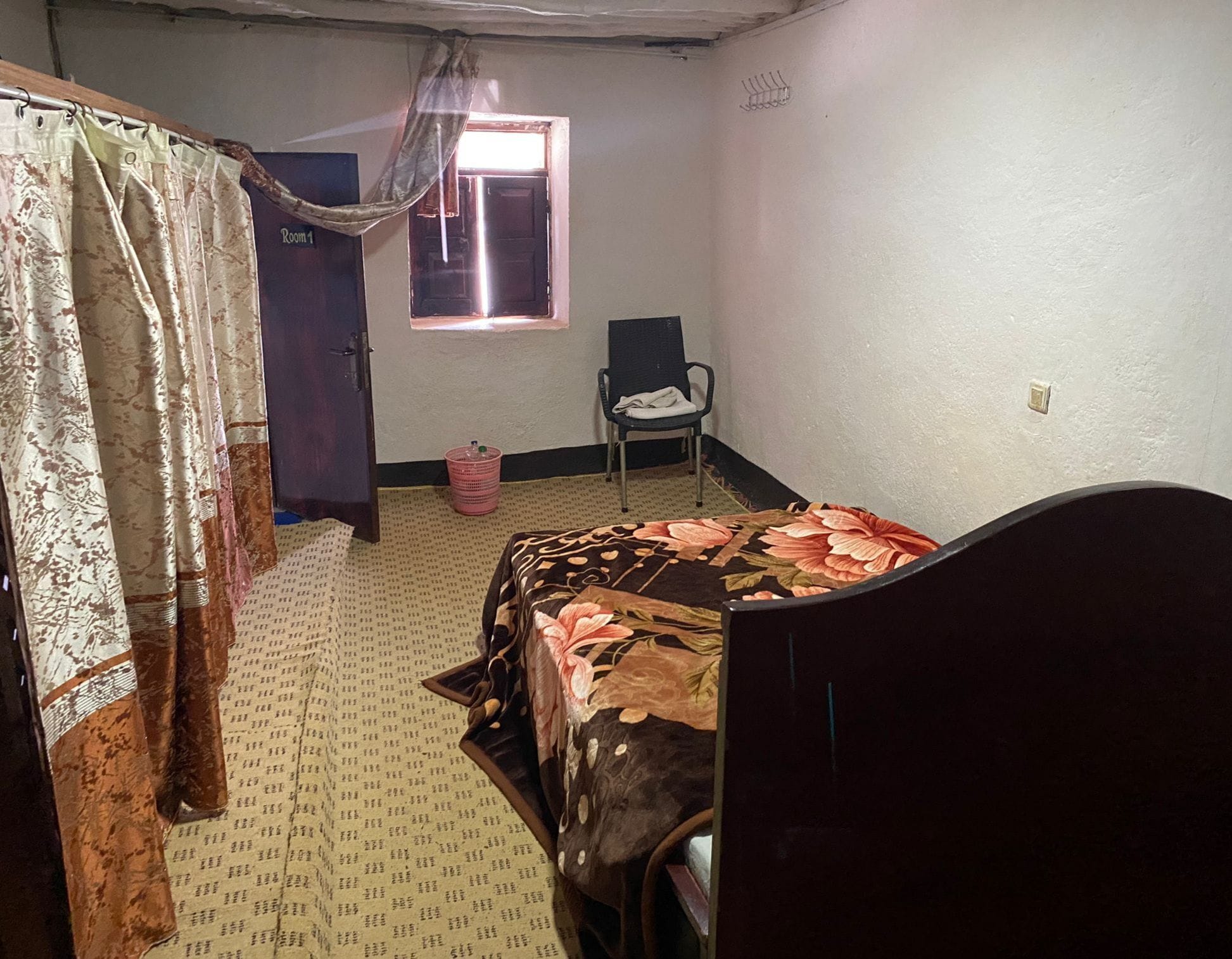 A bedroom with a bed, a chair, a window with curtains, and a door.