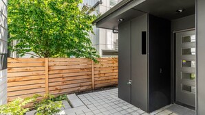 En modern byggnad med ett trästaket, en stenlagd uteplats och en svart dörr med flera fönster.