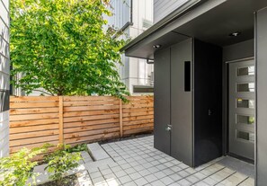 Un bâtiment moderne avec une clôture en bois, une terrasse pavée et une porte noire dotée de plusieurs fenêtres.