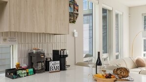 Ett modernt kök med en kaffestation, en matplats med ett vitt bord och utsikt över staden genom stora fönster.