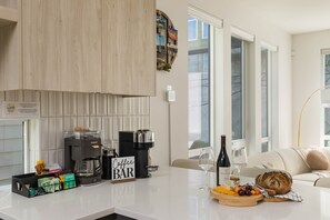 Une cuisine moderne dotée d’un coin café, d’un espace repas avec une table blanche et offrant une vue sur la ville grâce à de grandes fenêtres.
