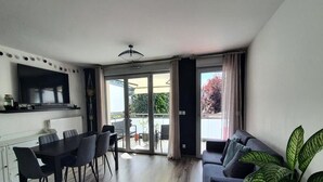 A modern living room with a dining area, a sofa, and a large plant. - Residence Le Clos Des Merisiers (Aix-les-Bains)