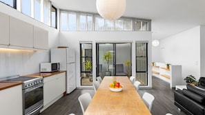 A modern kitchen with a dining area, featuring a wooden table with fruit, white cabinetry, and a large window. - Manyana Beach Escape (Manyana)
