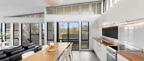 A modern kitchen with a wooden countertop, stainless steel appliances, and a dining area with a leather couch and white chairs.