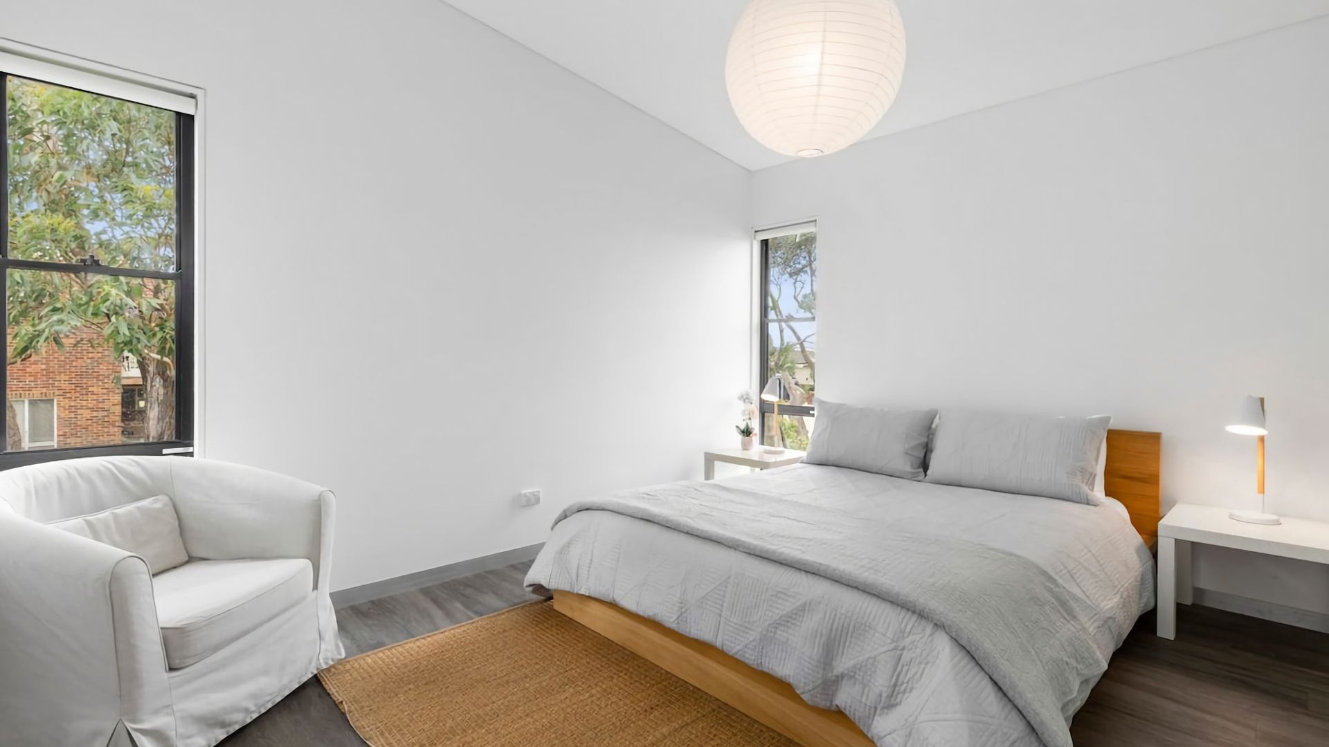 Una camera da letto moderna con un letto, una sedia, un comodino e una finestra che si affaccia sul verde.