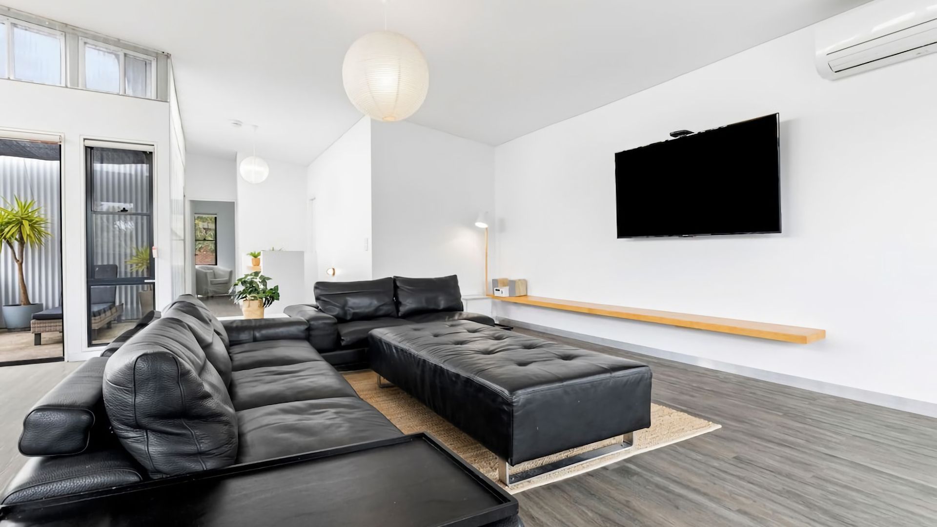 A modern living room with a sectional sofa, a flat-screen TV mounted on the wall, and a wooden bench.