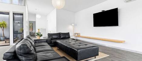 A modern living room with a sectional sofa, a flat-screen TV mounted on the wall, and a wooden bench.