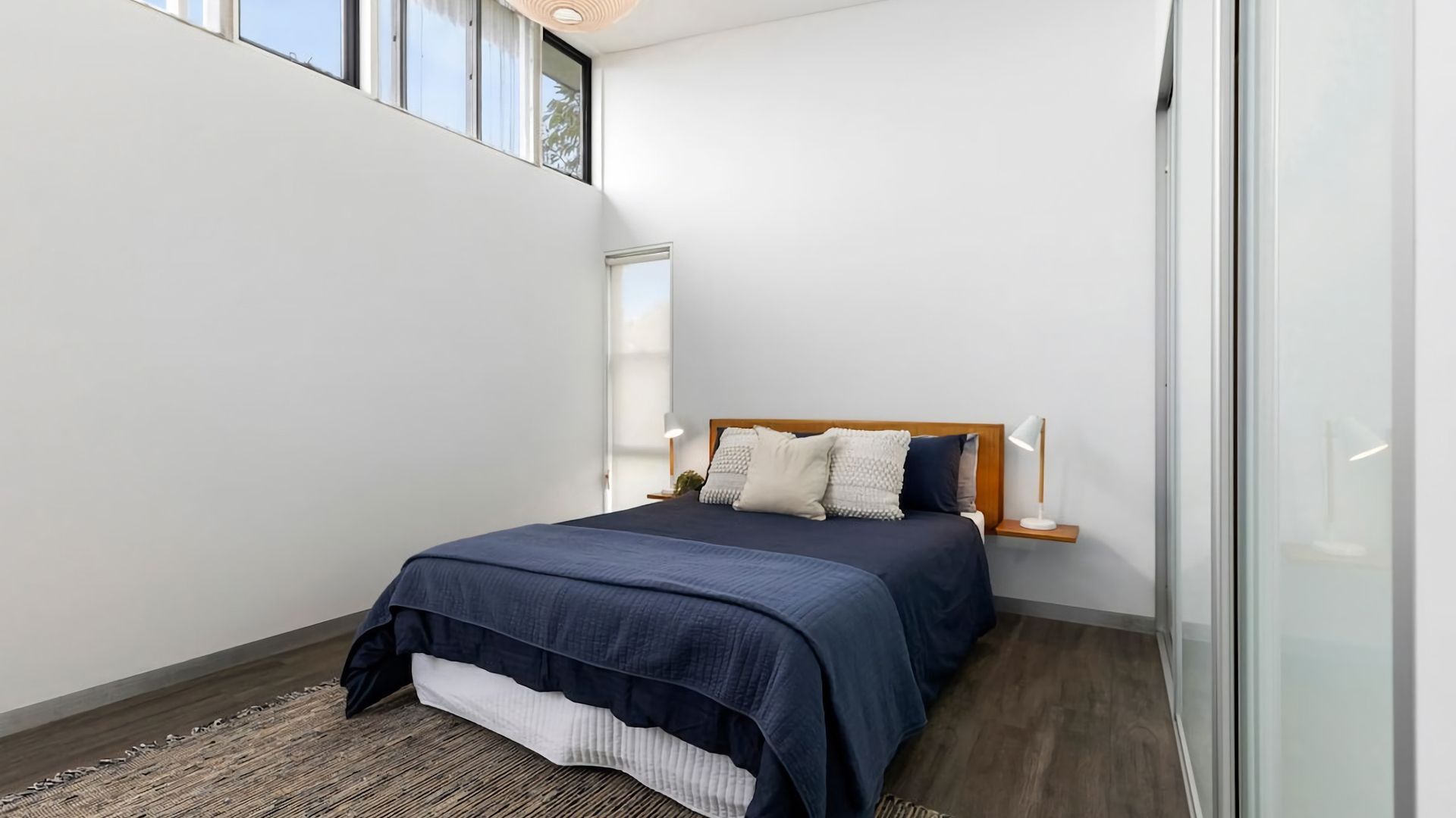A bedroom with a bed, bedside lamps, a wooden headboard, a window, and a glass door.