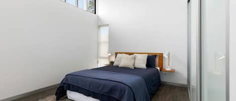 Une chambre à coucher avec un lit, des lampes de chevet, une tête de lit en bois, une fenêtre et une porte en verre.