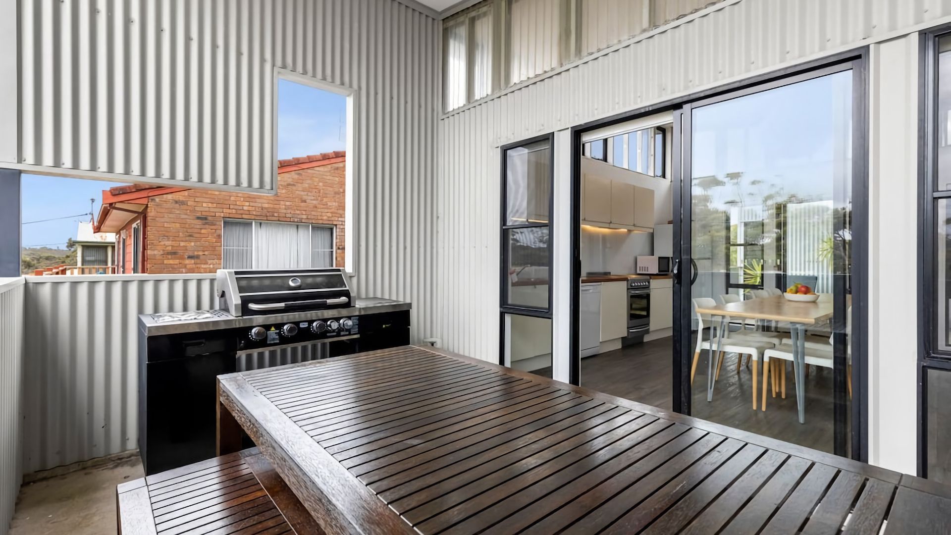 A modern outdoor kitchen with a grill, a wooden table, and a sliding glass door leading to a dining area.